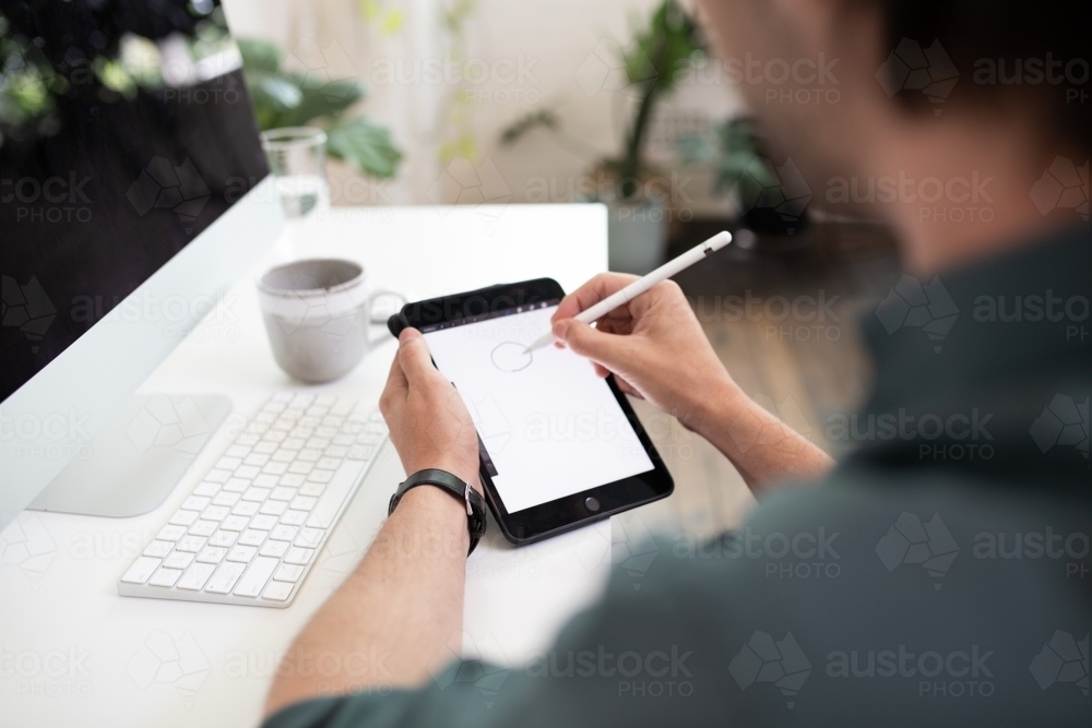Close-up of a man using a stylus pen on e-device. - Australian Stock Image