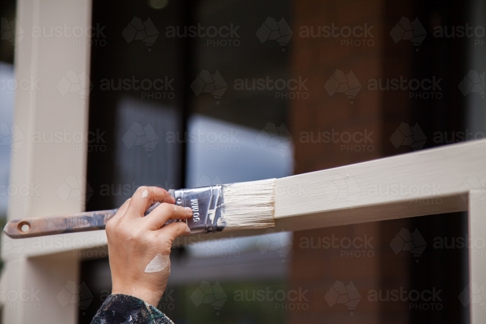 Close up of a painter painting handrails of a home cream colour - Australian Stock Image