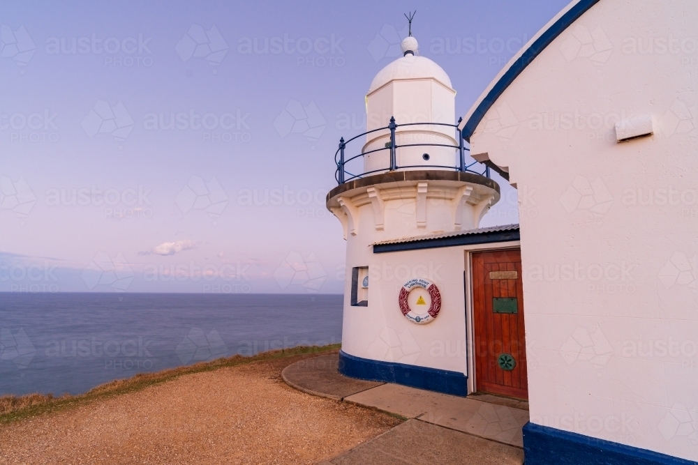 Close up of a short lighthouse sitting on top of a hill with a calm ocean in the background - Australian Stock Image