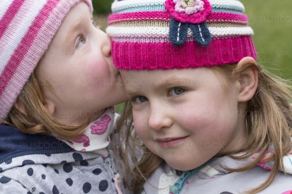 Close up of a six year old girl kissing her twin sister - Australian Stock Image