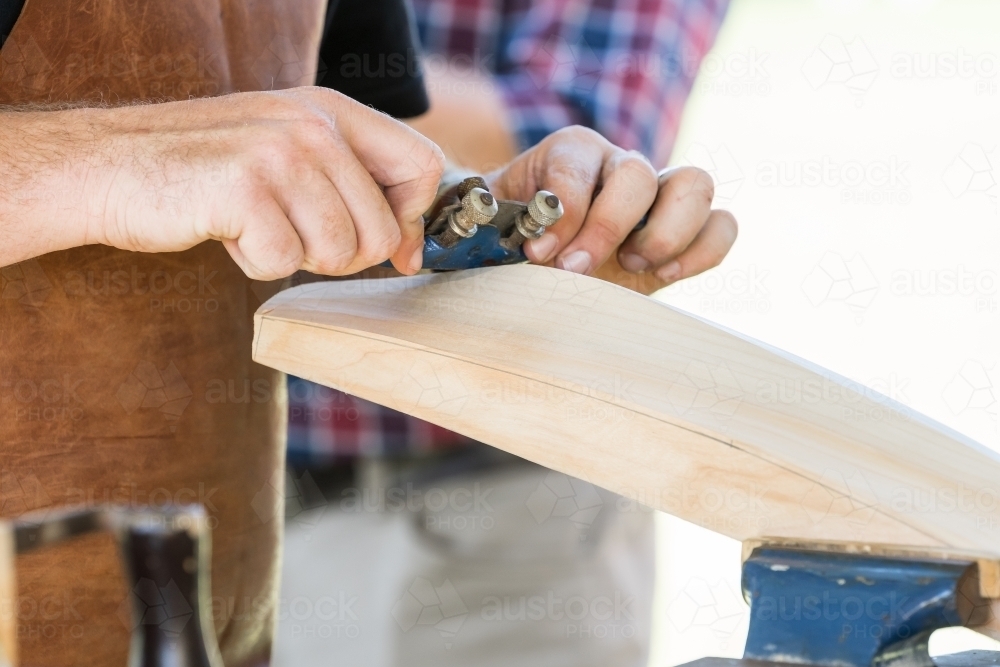 Close up of a tradesman's hands using a shaving tool over the back of cricket bat - Australian Stock Image