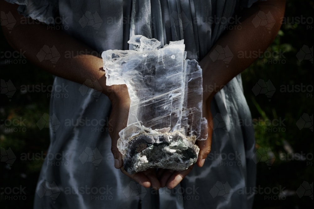 Close up of a woman holding a dark, selenite crystal on geode - Australian Stock Image