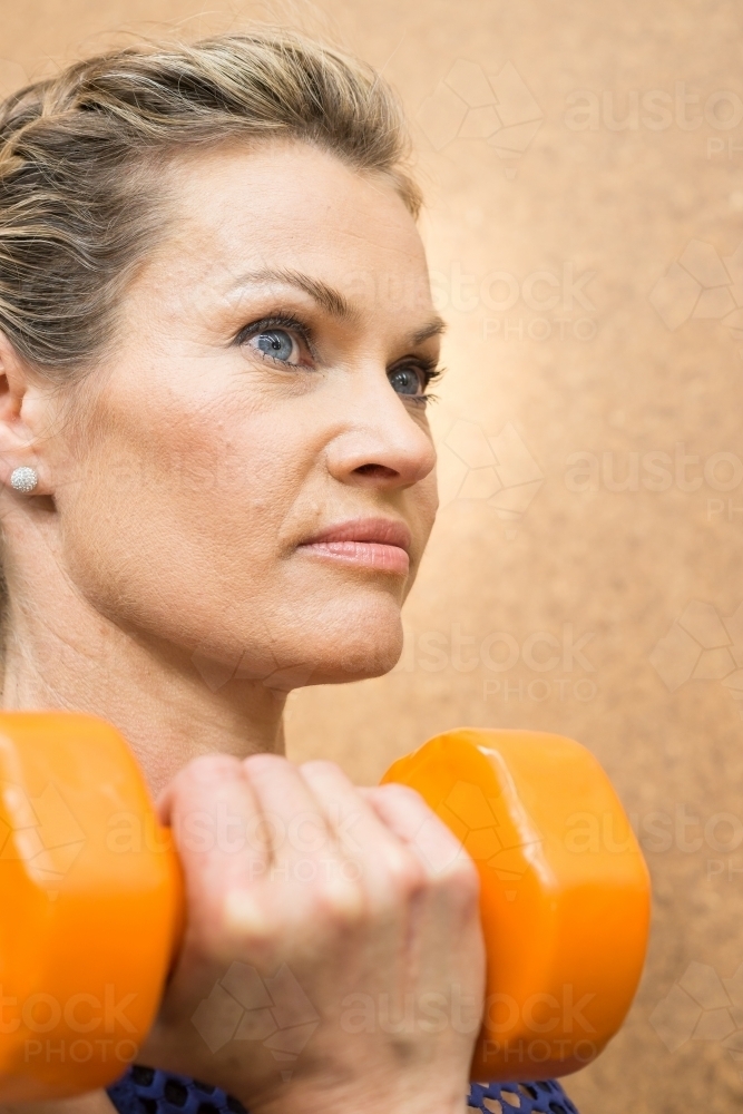 Close up of a woman lifting weights under her chin in a gym - Australian Stock Image
