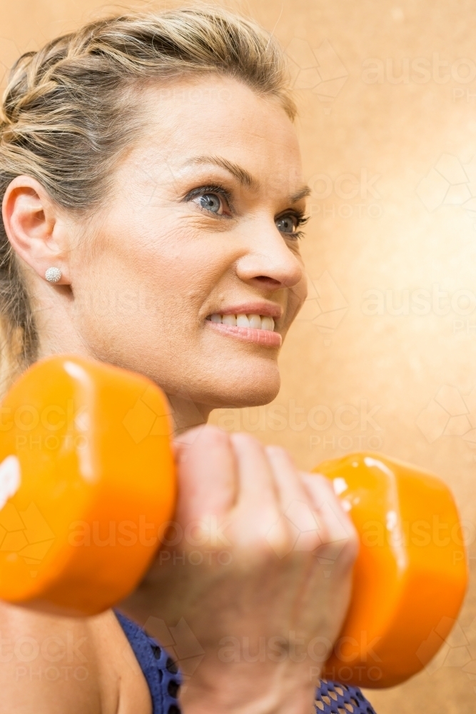 Close up of a woman lifting weights under her chin in a gym - Australian Stock Image