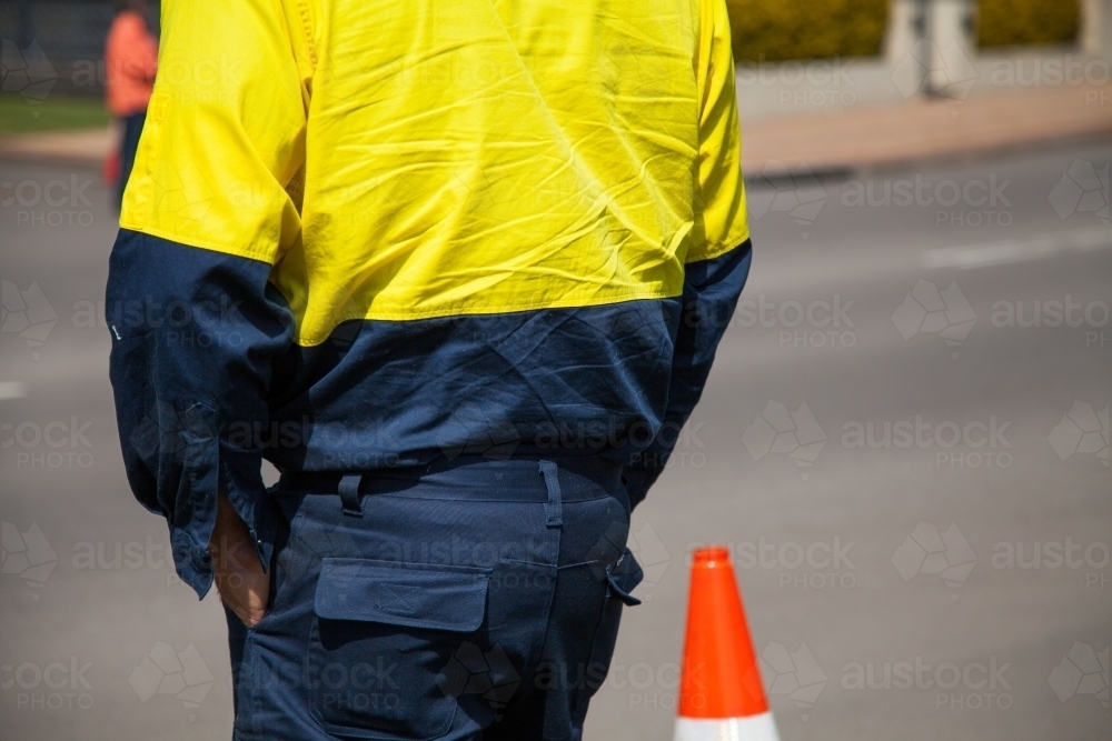 Close up of a worker in safety clothing standing beside a road cone - Australian Stock Image
