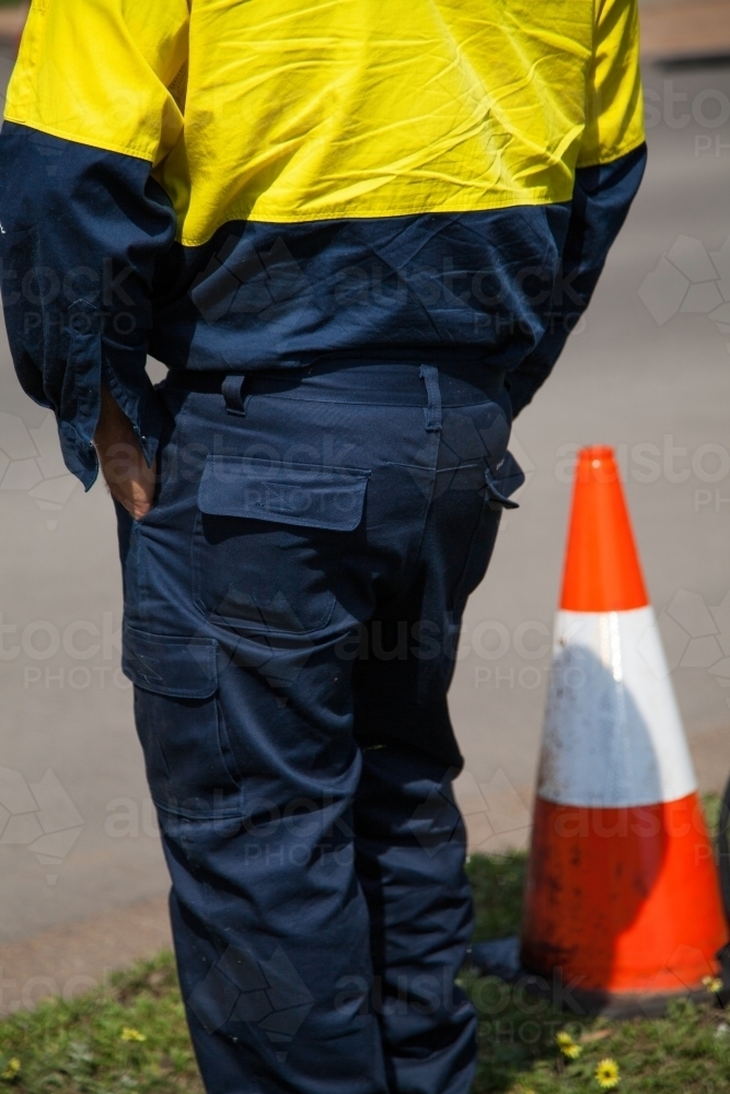 Close up of a worker in safety clothing standing beside a road cone - Australian Stock Image