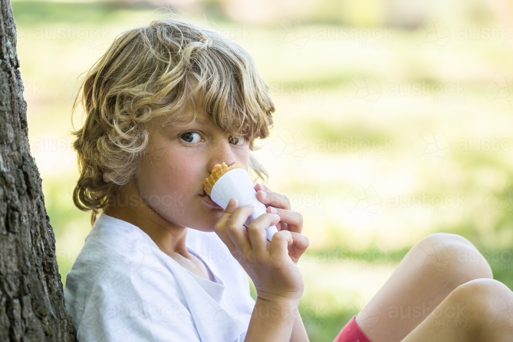 Close up of a young boy biting an ice cream cone - Australian Stock Image