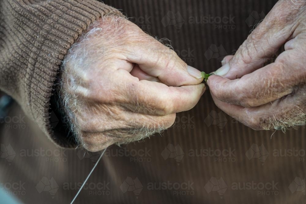 Close up of an old man's hands baiting a fishing hook - Australian Stock Image
