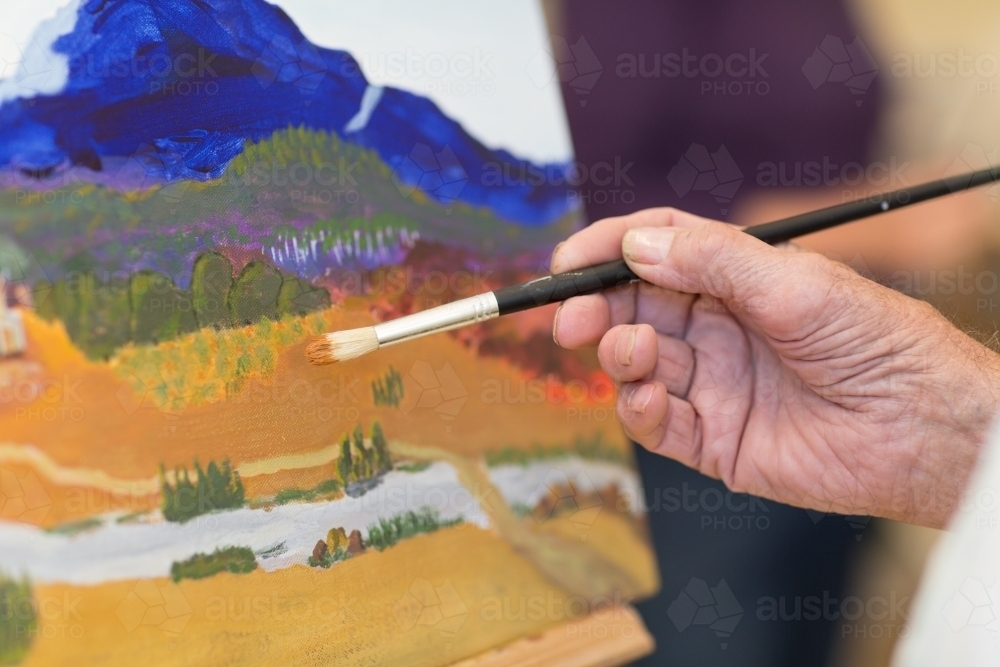 Close up of artist's hand holding paint brush with painting - Australian Stock Image