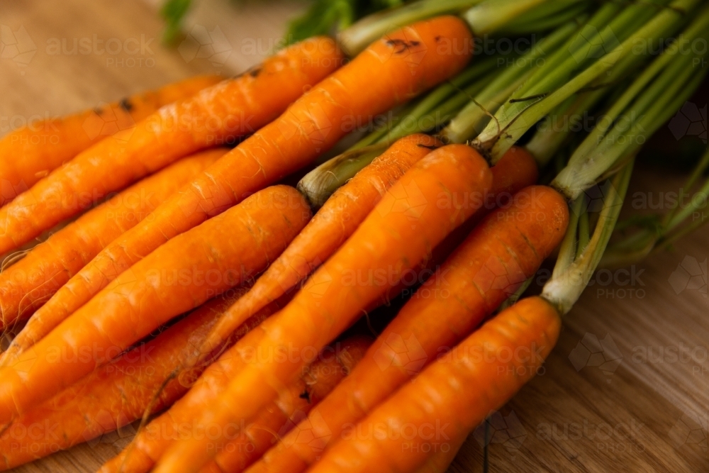 close up of baby carrots with carrot tops on a wooden table - Australian Stock Image