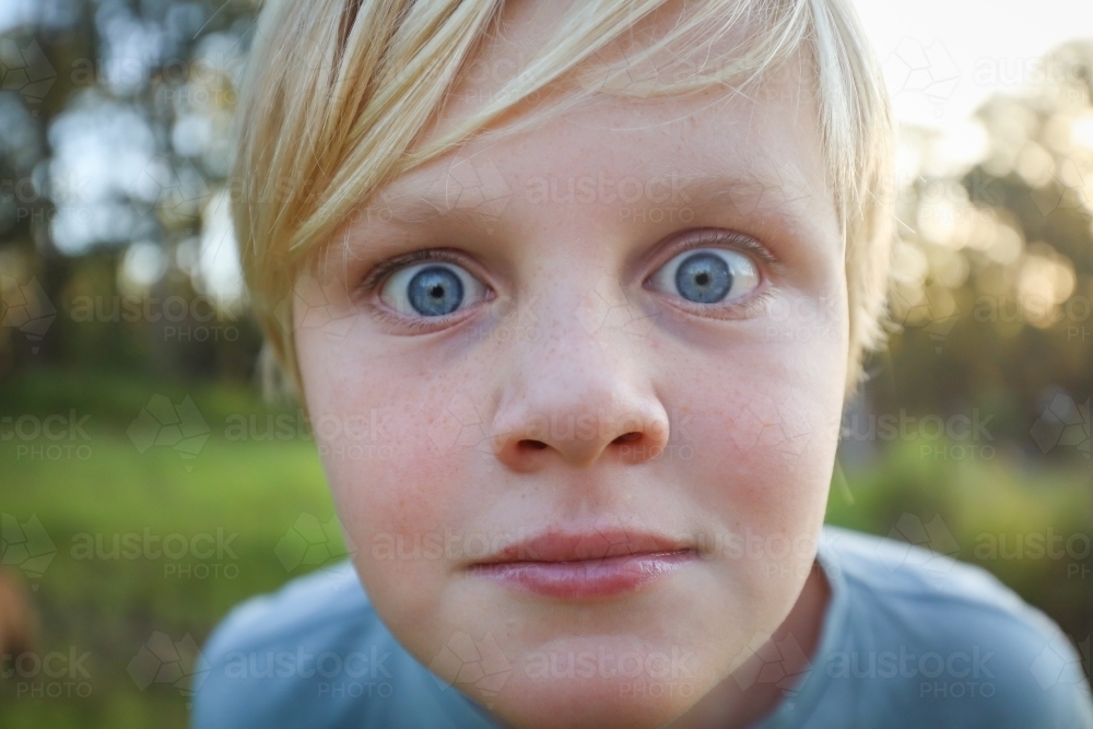 Close up of blonde boy with big blue eyes and freckles being silly - Australian Stock Image