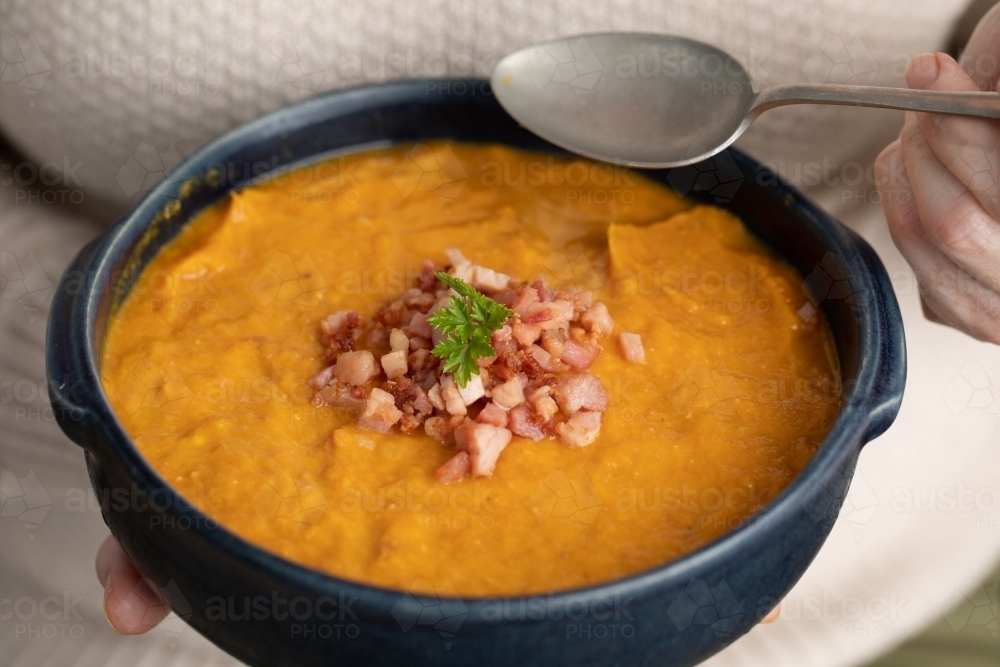 close up of blue bowl of pumpkin soup in lady hands and spoon - Australian Stock Image