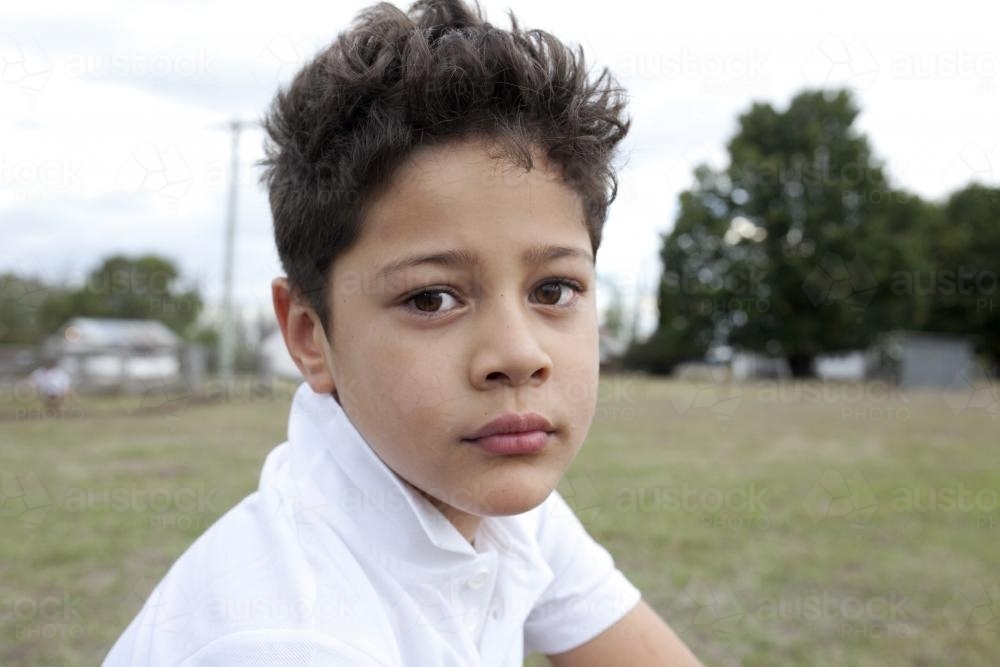 Close up of boy wearing white shirt outside looking thoughtful - Australian Stock Image