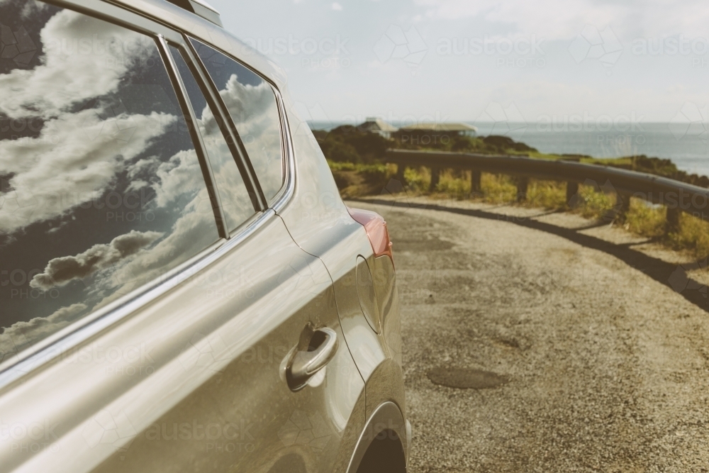 Close up of bronze coloured car parked on side of road with sky and clouds reflected in the window - Australian Stock Image