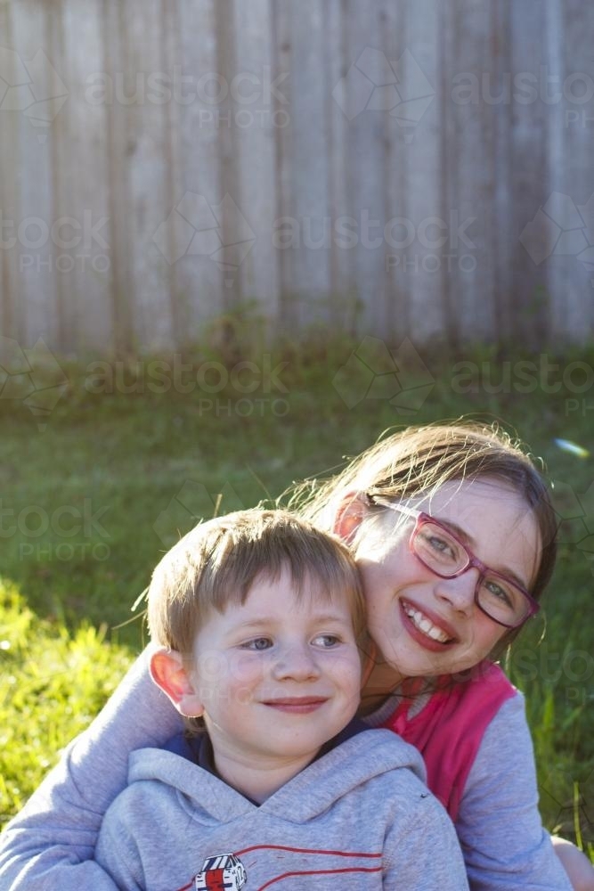 Close up of brother and sister sitting together in afternoon sun - Australian Stock Image
