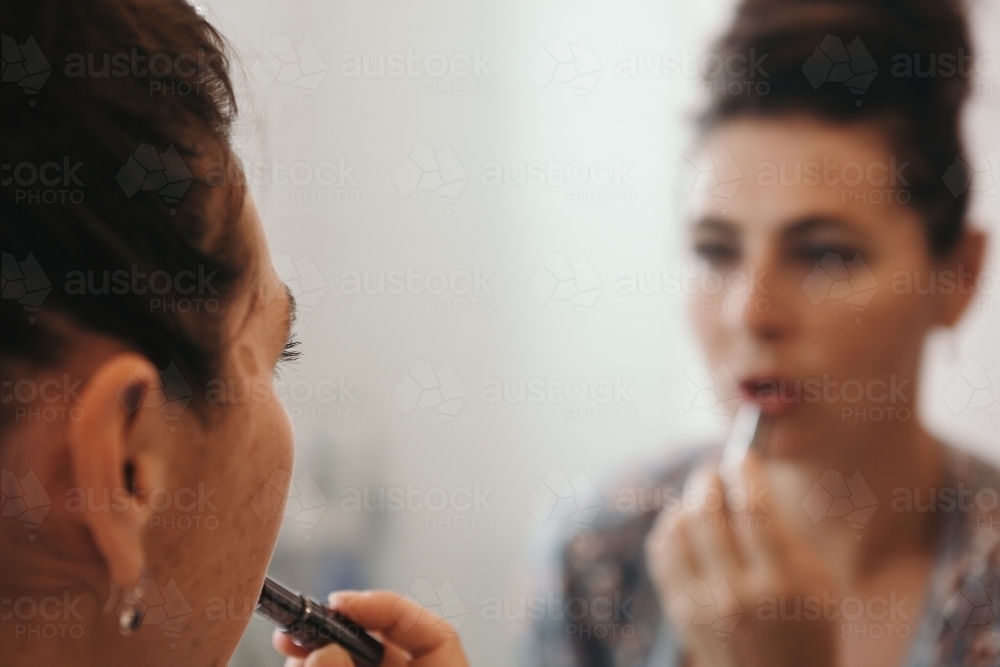 Close up of brunette woman applying makeup with blurred mirror reflection - Australian Stock Image