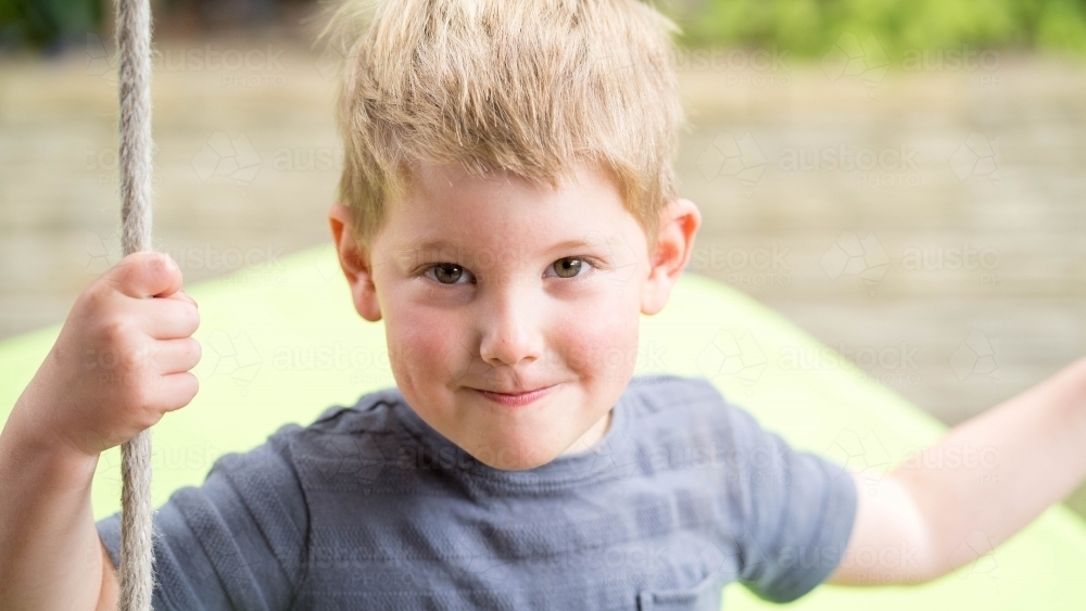 Close up of cheeky three year old on swing - Australian Stock Image