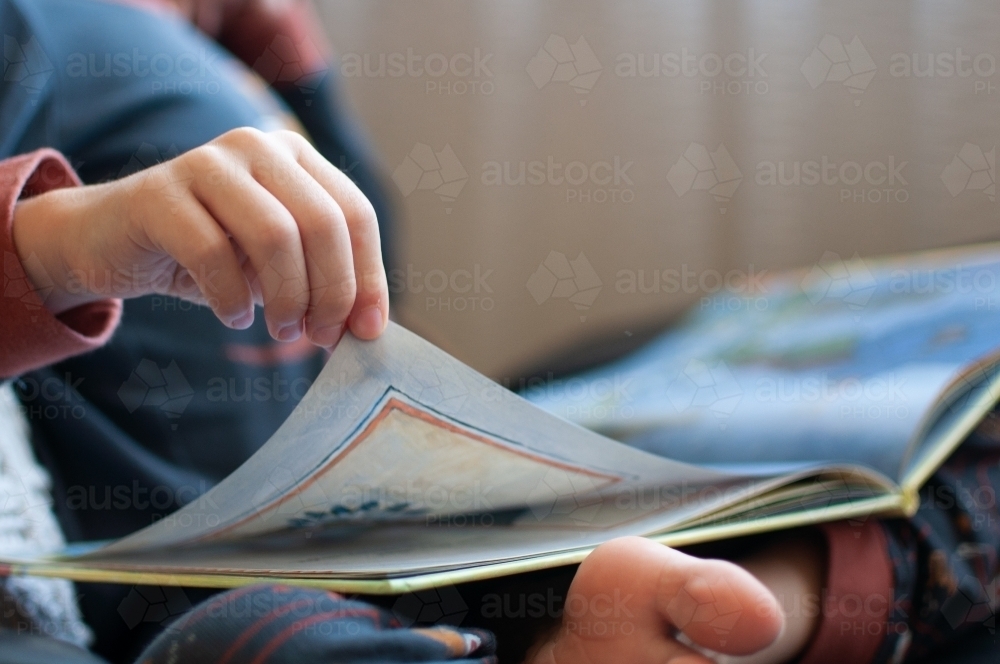 Close up of child's hand turning page of book - Australian Stock Image