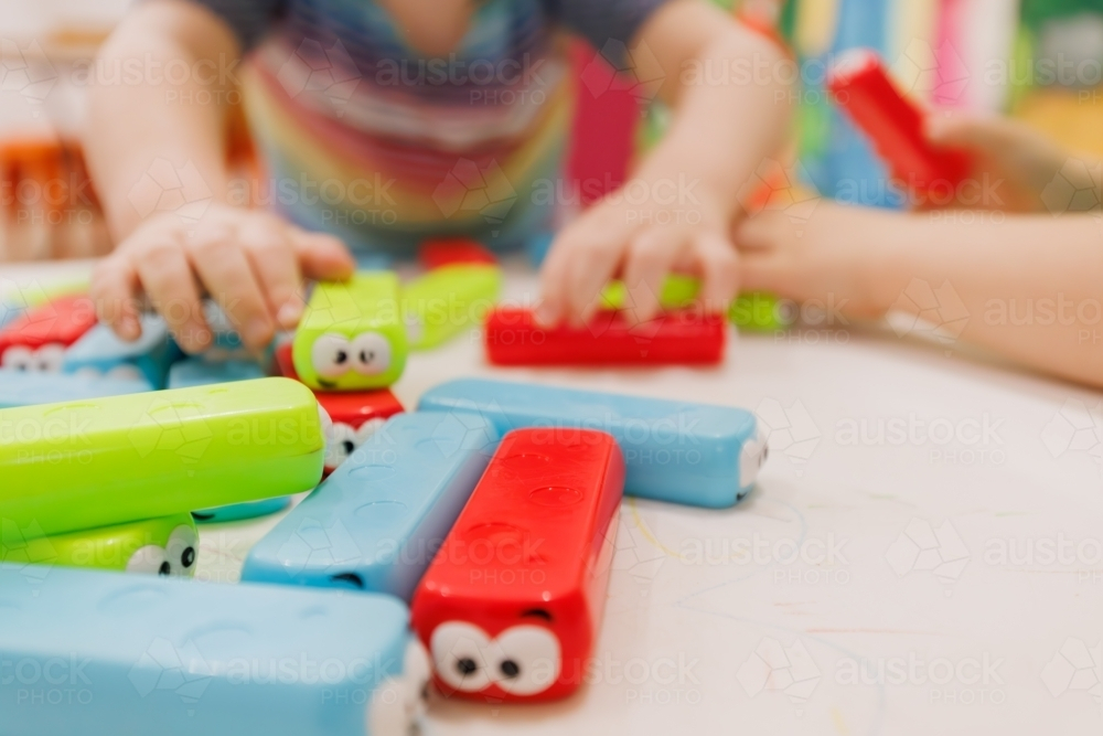 Close up of child's hands building with brightly coloured blocks with googly eyes - Australian Stock Image