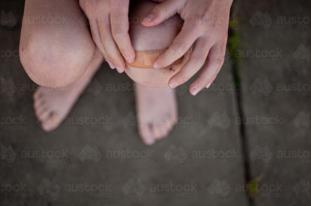 Close up of child's hands putting plaster on grazed knee - Australian Stock Image