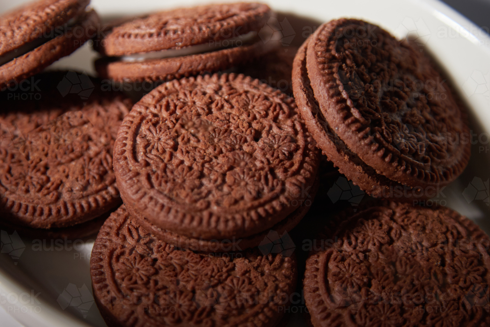 close up of chocolate cream biscuits on white plate - Australian Stock Image