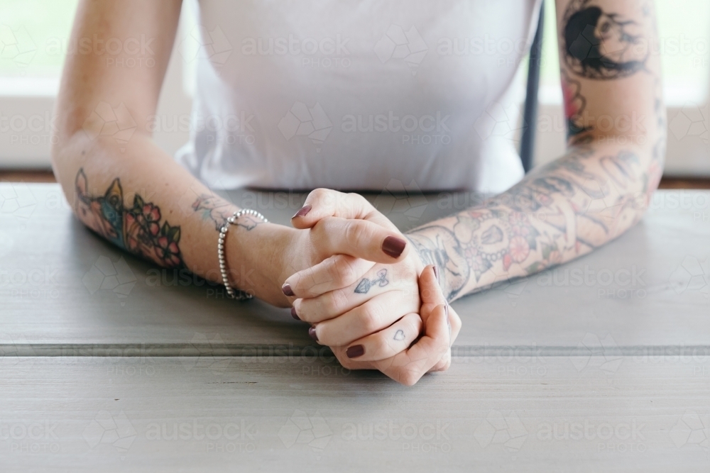 Close up of clasped female hands with tattoos - Australian Stock Image