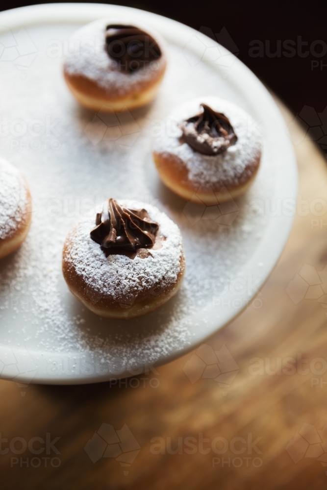 Close up of delicious chocolate topped donuts on a vintage cake stand from overhead - Australian Stock Image