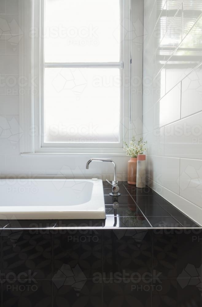 Close up of designer black tiled bath hob with white tiled wall and window behind - Australian Stock Image