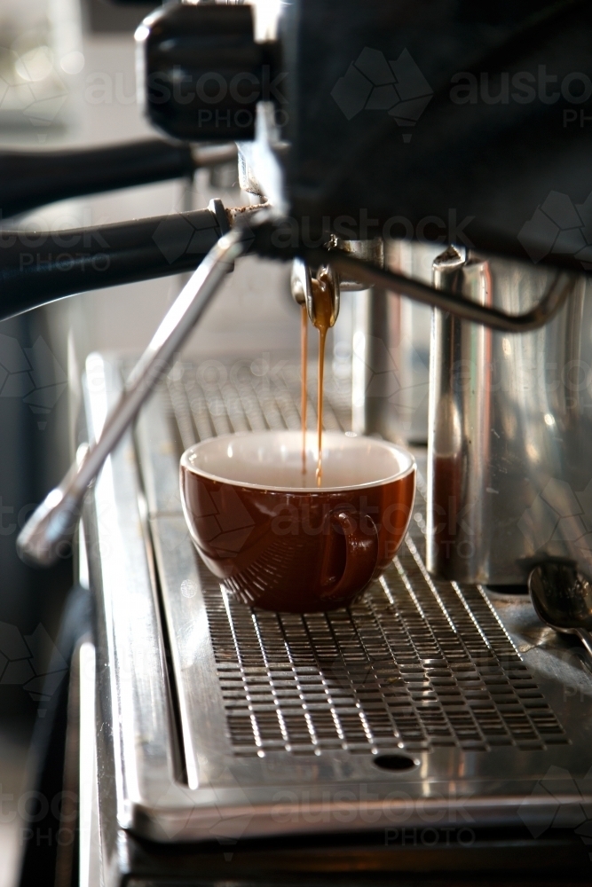Close up of espresso coffee pouring into cup from coffee machine - Australian Stock Image