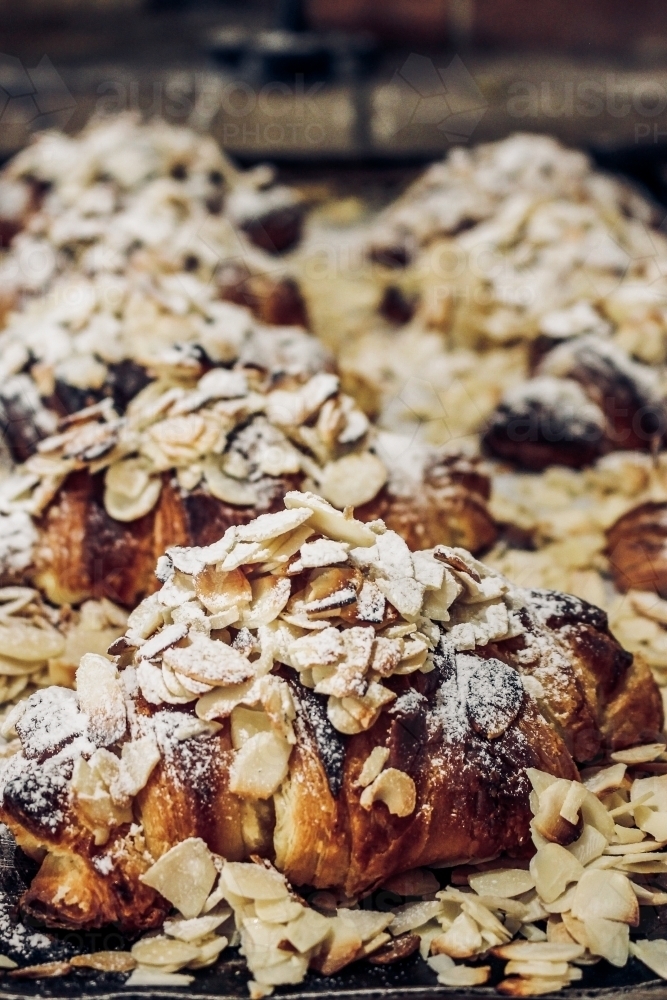 Close up of freshly baked almond croissants dusted with shaved almonds and icing sugar - Australian Stock Image