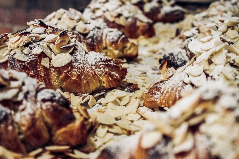 Close up of freshly baked almond croissants dusted with shaved almonds and icing sugar - Australian Stock Image