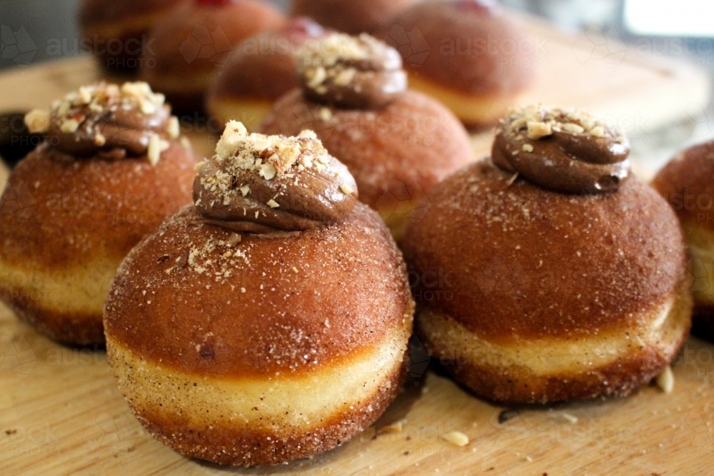 Close up of freshly baked doughnuts filled with chocolate ganache and sprinkled with hazelnuts - Australian Stock Image