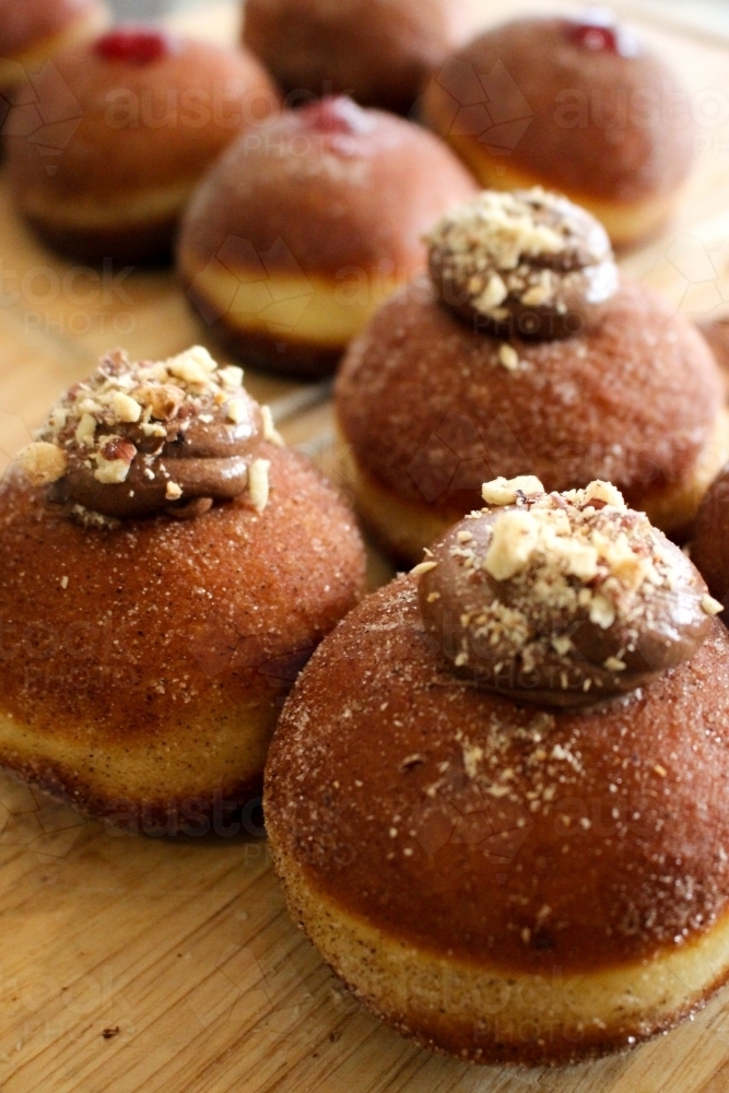 Close up of freshly baked doughnuts filled with chocolate ganache and sprinkled with hazelnuts - Australian Stock Image