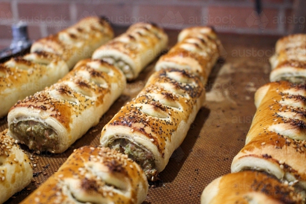Close up of freshly baked sausage rolls lined up on a baking tray - Australian Stock Image
