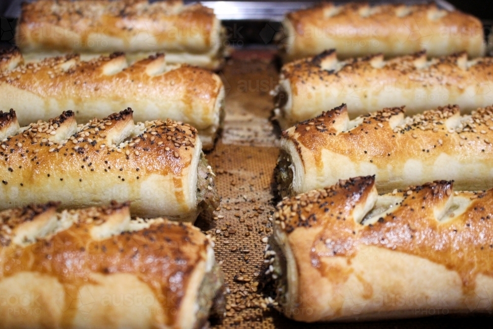Close up of freshly baked sausage rolls lined up on a baking tray - Australian Stock Image