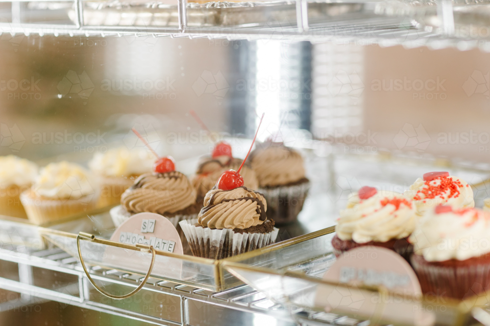 Close-up of freshly made cupcakes showcased in a glass bakery display - Australian Stock Image