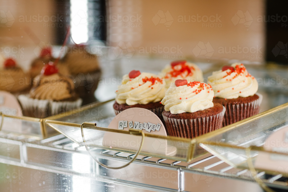 Close-up of freshly made red velvet cupcakes showcased in a glass bakery display - Australian Stock Image