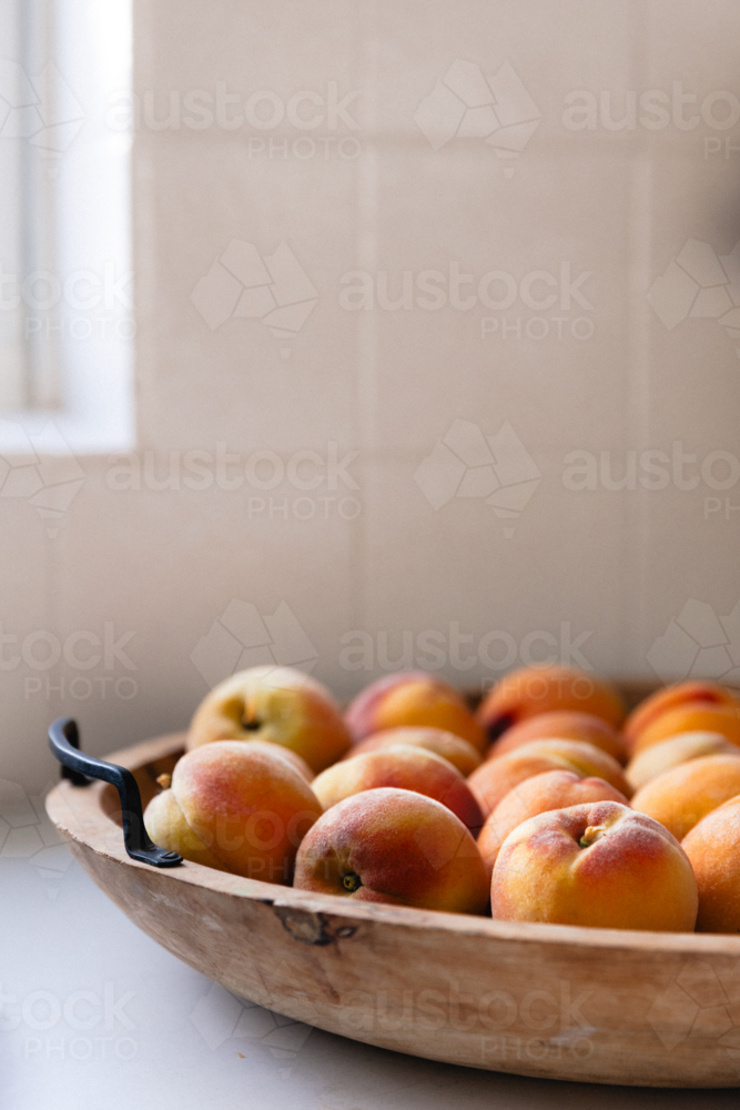 Close up of freshly picked ripe peaches in a wooden bowl on white kitchen bench - Australian Stock Image