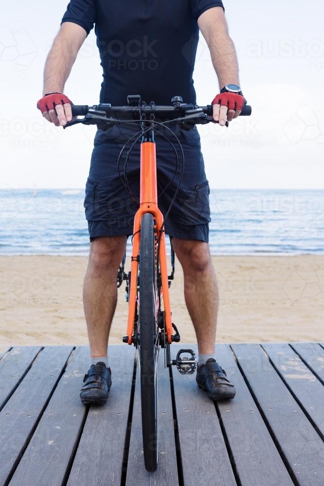 Close up of front on man standing with bicycle at the beach - Australian Stock Image