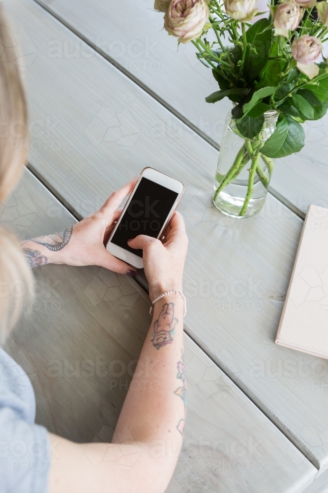 Close up of girl with tattoos using her mobile device at home - Australian Stock Image