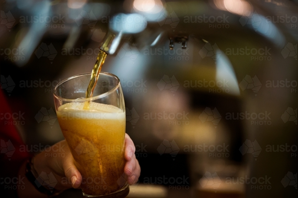 Close up of glass with on tap drink pouring into glass at pub - Australian Stock Image