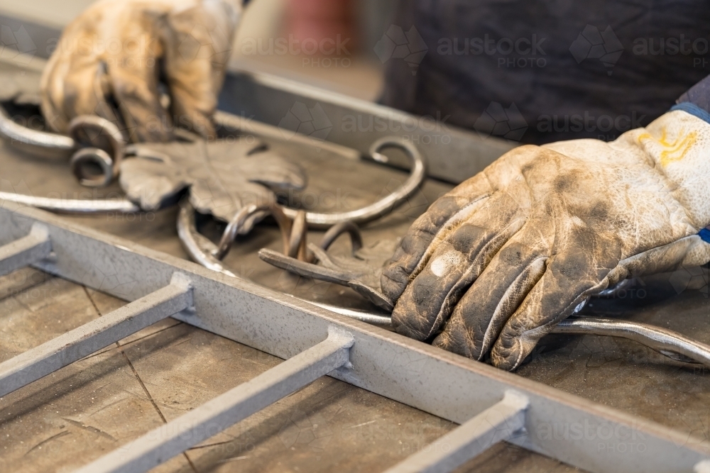 Close up of gloved hands arranging ornate metal pieces of a gate - Australian Stock Image