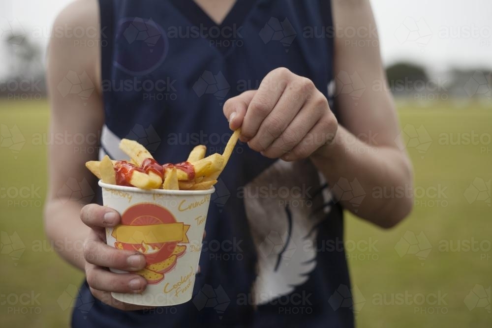 Close up of grassroots Footy player eating hot chips - Australian Stock Image