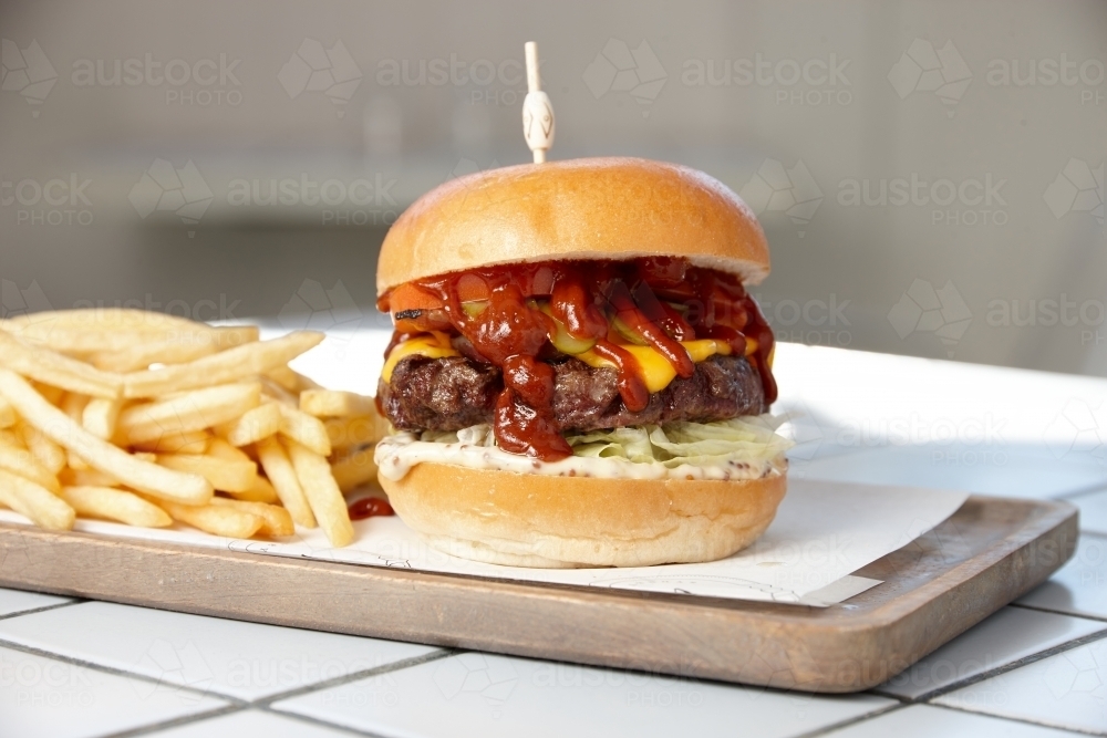 Close up of hamburger and fries on board - Australian Stock Image
