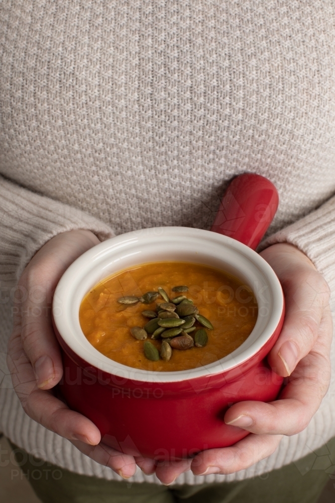 close up of hands holding bowl of pumpkin soup - Australian Stock Image