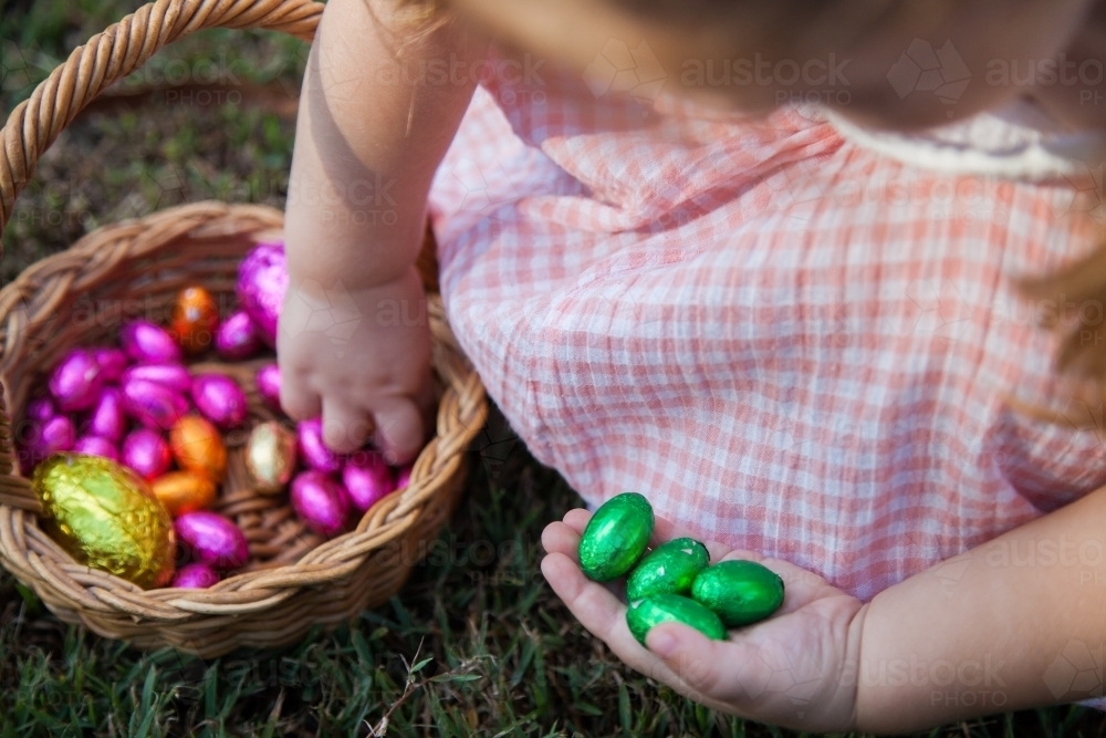 Close up of little girl taking coloured Easter eggs out of Easter egg hunt basket - Australian Stock Image