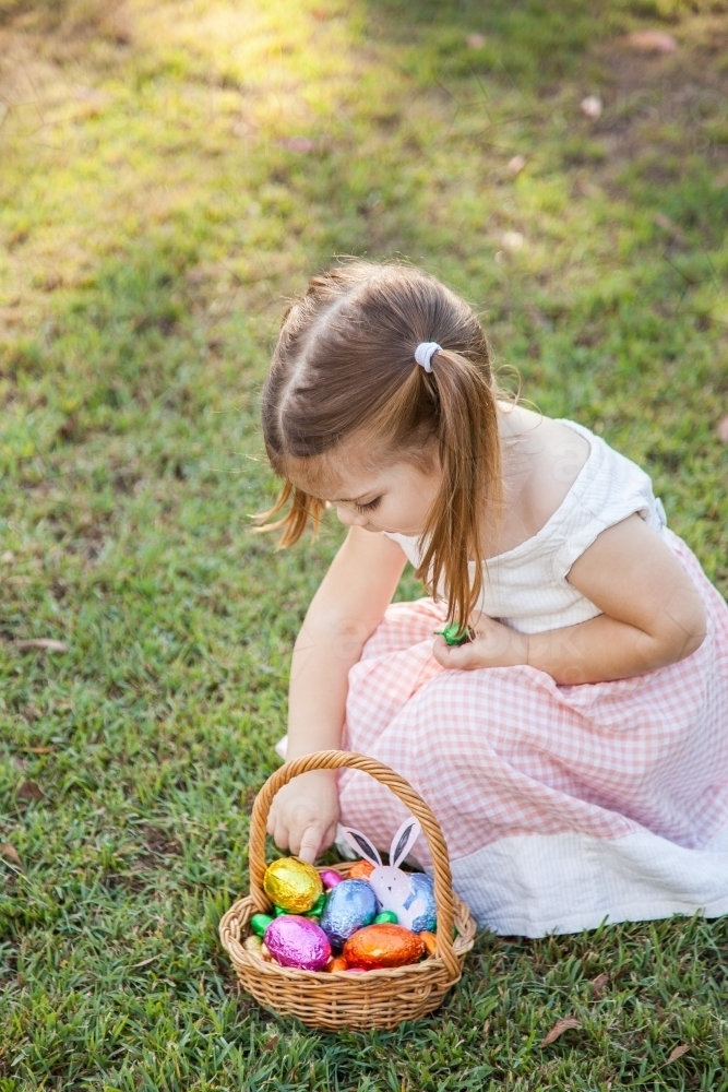 Close up of little girl taking coloured Easter eggs out of Easter egg hunt basket - Australian Stock Image