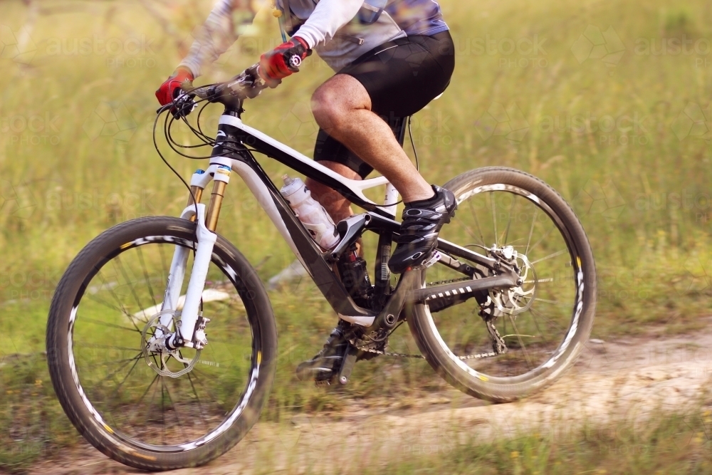 Close up of male cyclist riding pushbike on trail through paddock - Australian Stock Image