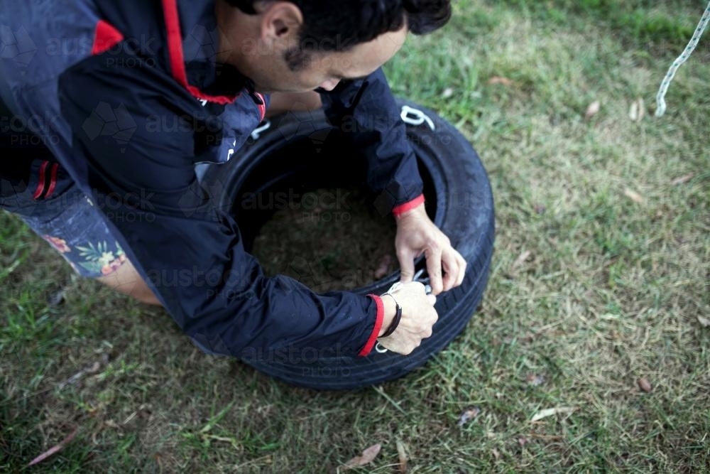 Close up of man making a tyre swing in country backyard - Australian Stock Image