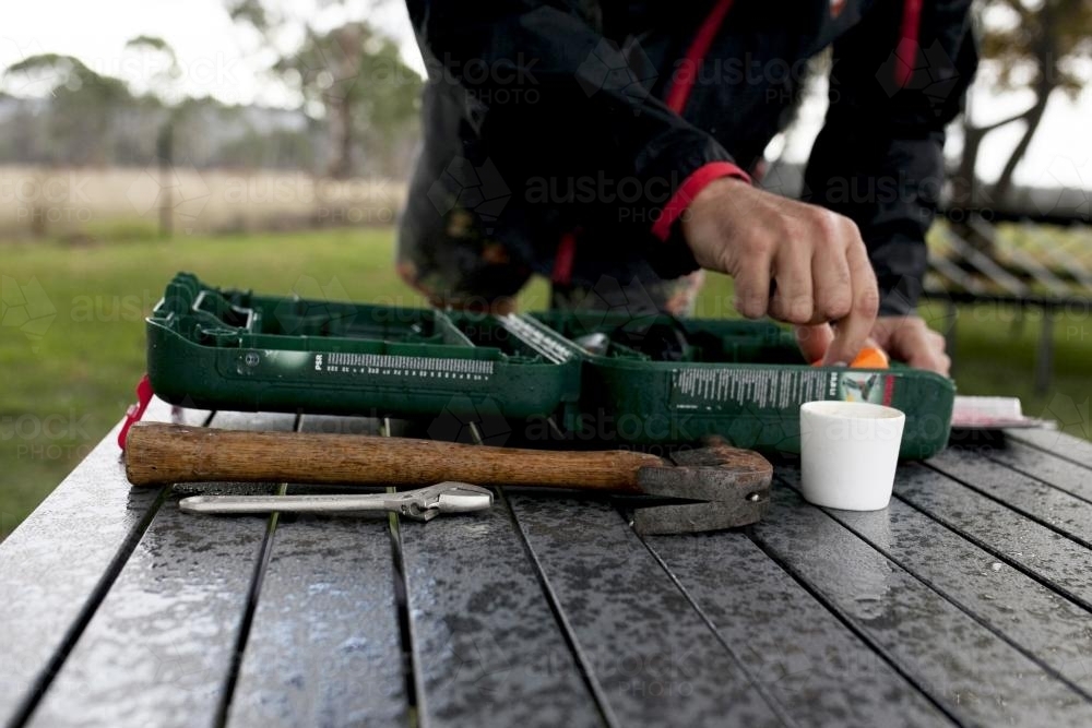 Close up of man with tool kit on table in country backyard - Australian Stock Image
